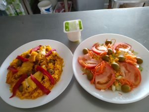 Variado menú nutritivo para adultos mayores: paella con pimientos, pescado aceitunas, ensalada mixta con lechuga y tomates más postre.