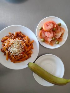Comida equilibrada para la nutrición en la tercera edad: macarrones con queso, una ensalada de tomate y un plátano de postre.