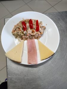 Plato colorido que promueve la salud en la vejez: ensaladilla rusa con pimientos acompañada de fiambre y queso.
